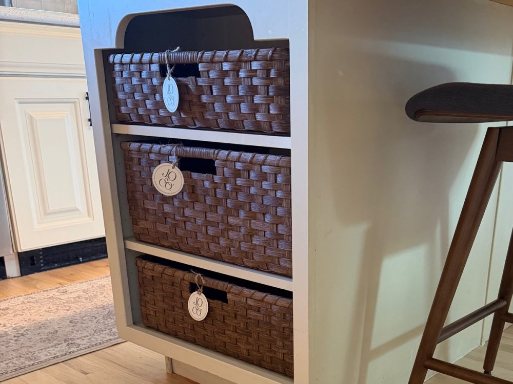 Three handwoven storage baskets, each tagged Jo & Co., filling the open end of a kitchen island