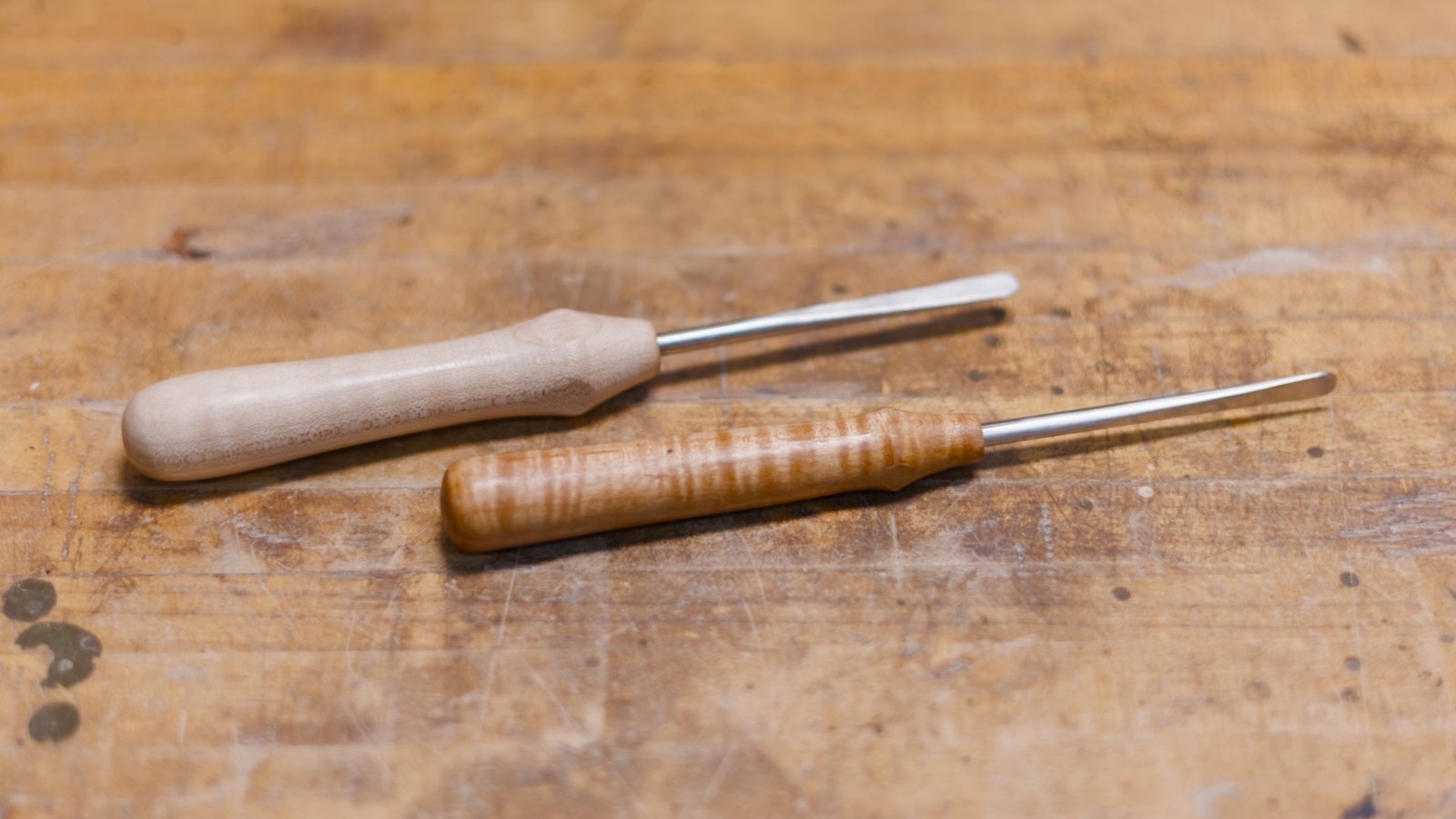 Two flat-tip basket weaving tools with maple handles on a workbench